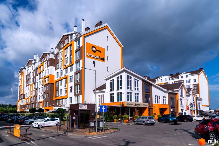 Новобудова Orange Park з яскравим фасадом у біло-коричнево-помаранчевих тонах. На території комплексу розташована парковка та в'їзна група.