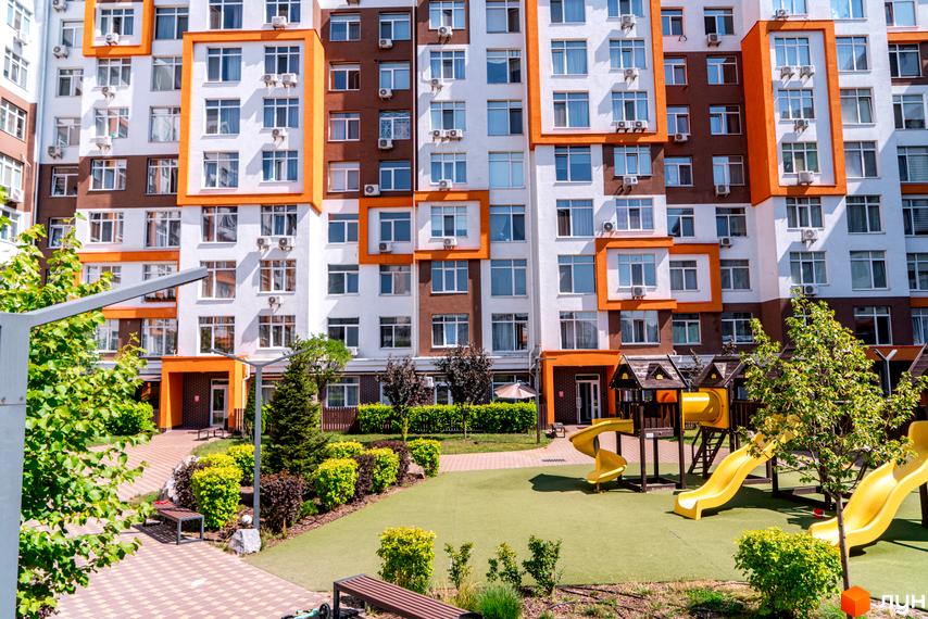 Житловий комплекс Orange Park: фасади будівель з помаранчевими елементами та прибудинкова територія з дитячим майданчиком. Зовнішній вигляд новобудови та її інфраструктура.