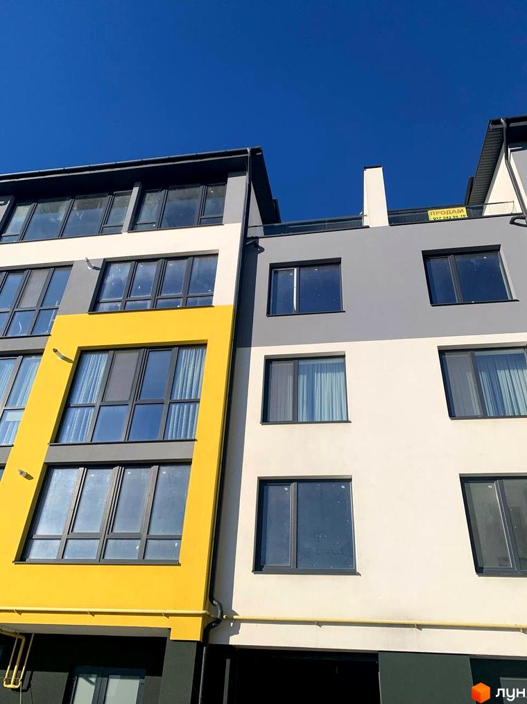 Зовнішній вигляд будинку ЖК ПАНОРАМА з жовтим фасадом та великими вікнами на фоні блакитного неба. Житловий комплекс знаходиться на етапі будівництва.