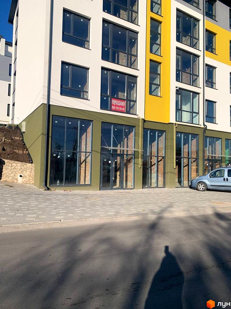 Фасад багатоповерхового будинку ЖК ПАНОРАМА з великими вікнами та скляними вхідними групами. Перед будинком асфальтована дорога та тротуар з бруківки.