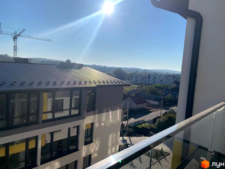 Вид на будівлі ЖК ПАНОРАМА з балкону. Навколо будинку видно інші будівлі та зелені насадження.