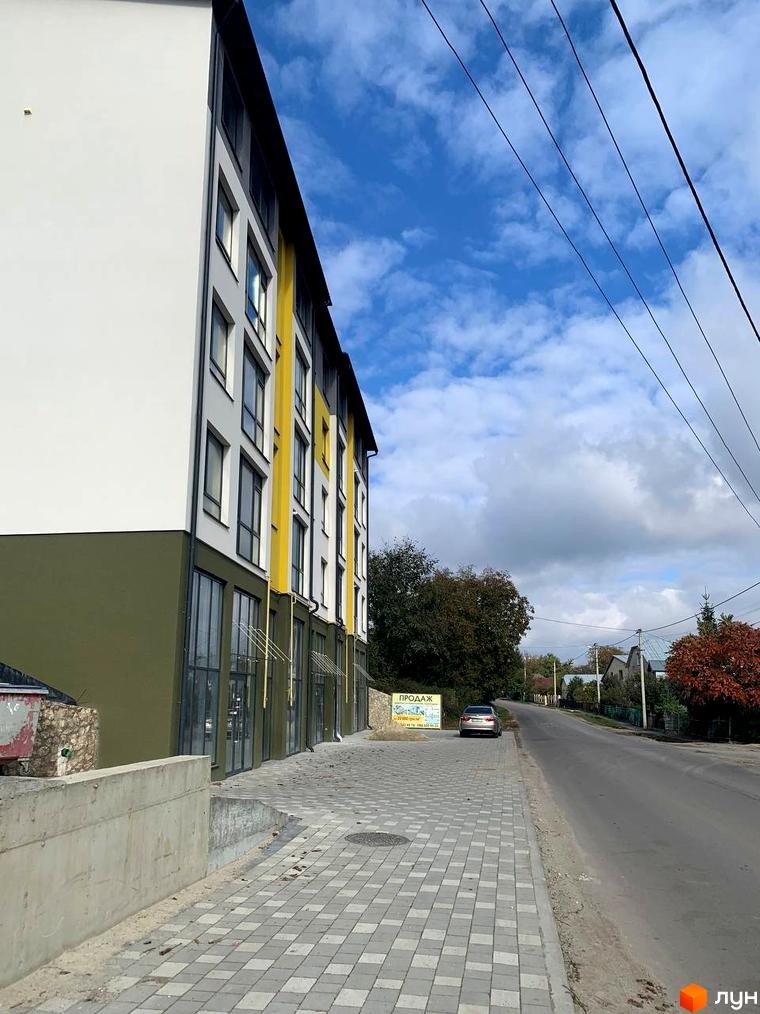 Багатоповерхова будівля ЖК ПАНОРАМА з фасадом у біло-жовтих тонах. На передньому плані тротуар з бруківки та дорога.