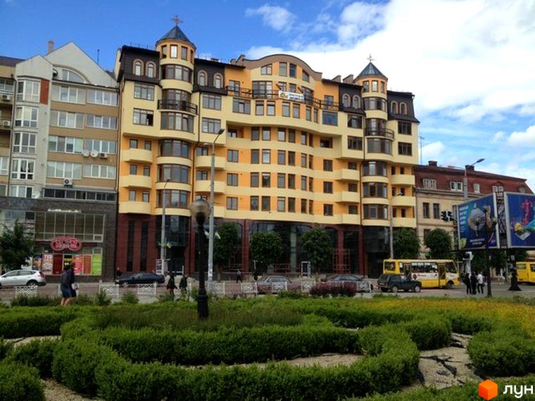 Зовнішній вигляд будинку по вулиці Незалежності, 87. Багатоповерхова будівля з жовтим фасадом та великими вікнами, навколо зелені насадження.
