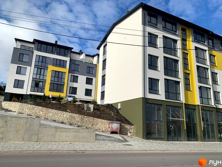 Багатоповерховий будинок ЖК ПАНОРАМА з панорамними вікнами та фасадом у білих, сірих та жовтих кольорах. На передньому плані – дорога та прибудинкова територія.
