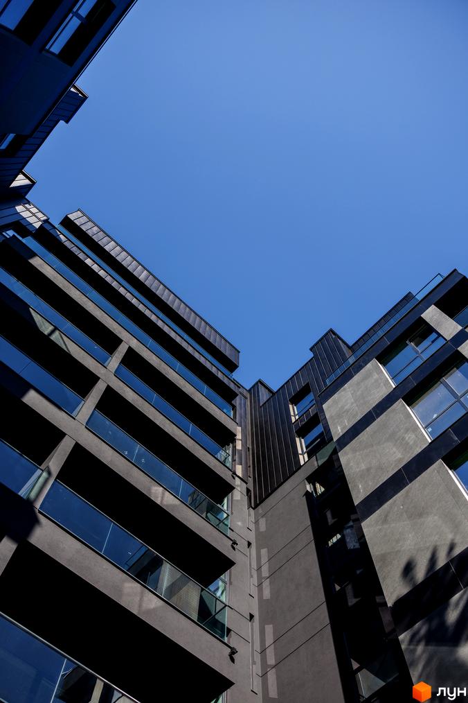 Фасад житлового комплексу Avalon Prime з скляними балконами та темними панелями на тлі блакитного неба. Архітектура новобудови.