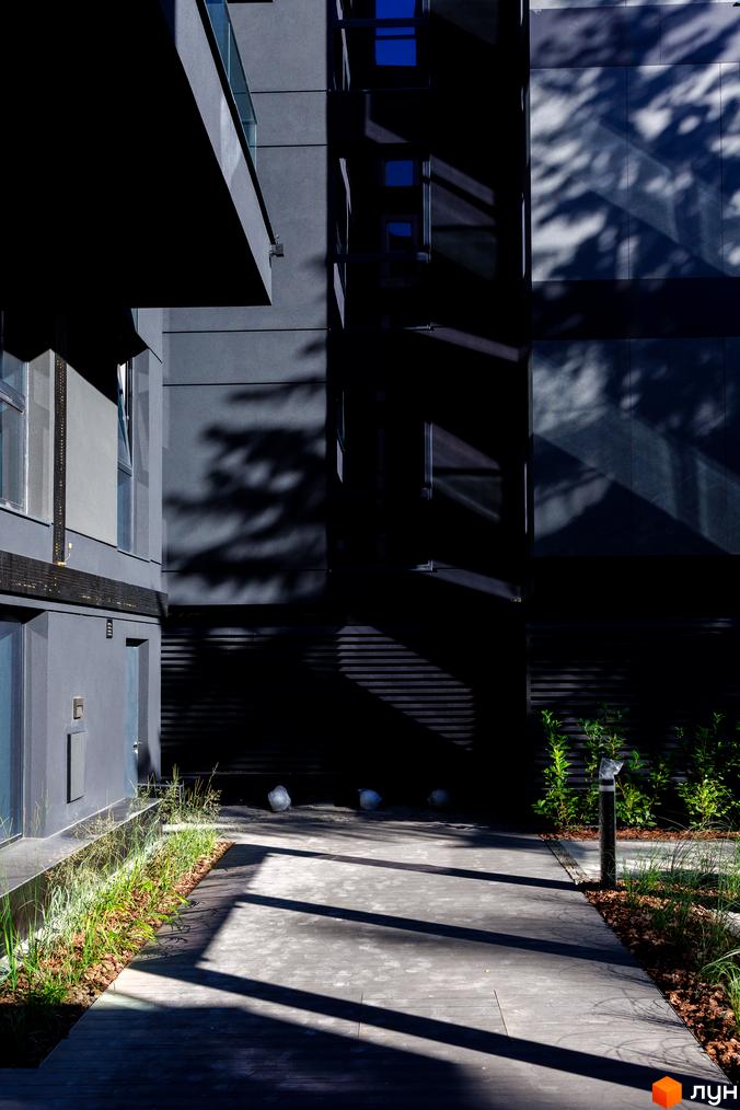 Зовнішній вигляд будинку ЖК Avalon Prime з темними фасадами та скляними елементами, прибудинкова територія з дерев'яною терасою та зеленню.