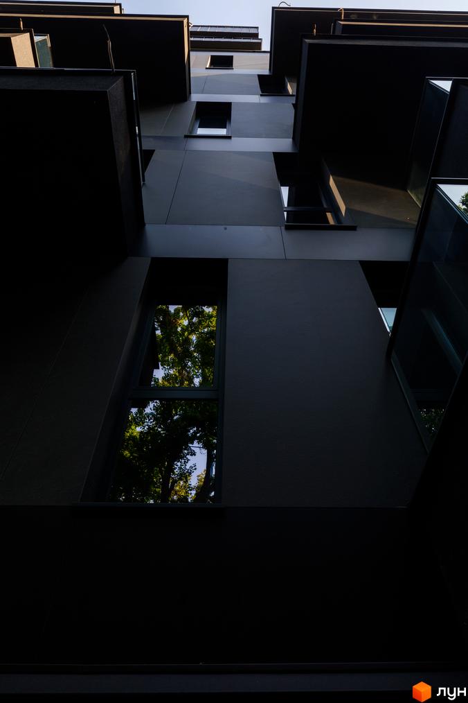 Фасад житлового комплексу Avalon Prime з темними панелями та великими вікнами, що відбивають зелені дерева.