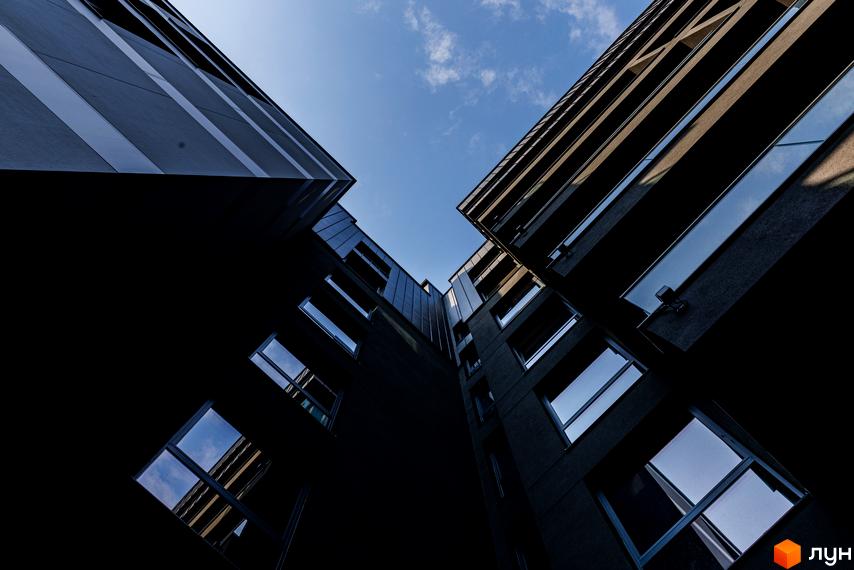 Зовнішній вигляд житлового комплексу Avalon Prime з темними фасадами та великими вікнами на тлі блакитного неба з хмарами.