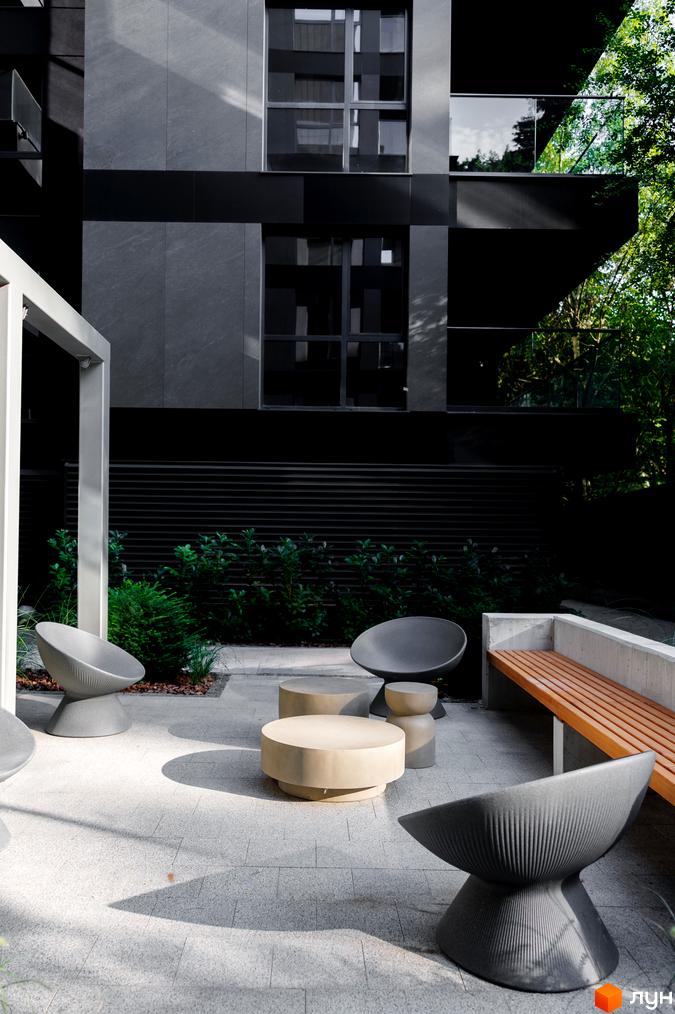 Житловий комплекс Avalon Prime з сірими фасадами та зонами відпочинку з кріслами та лавкою.