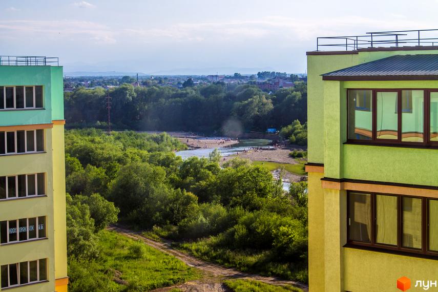 Фотографія фасаду Новобудови Веселка річкова з вікнами та балконами. На задньому плані річка, дерева та міський пейзаж.