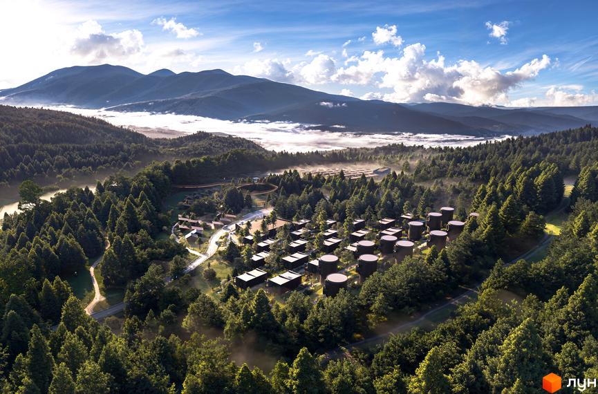 Вид зверху на Котеджне містечко Малахіт серед лісу з будинками різної форми. На задньому плані гори в тумані.