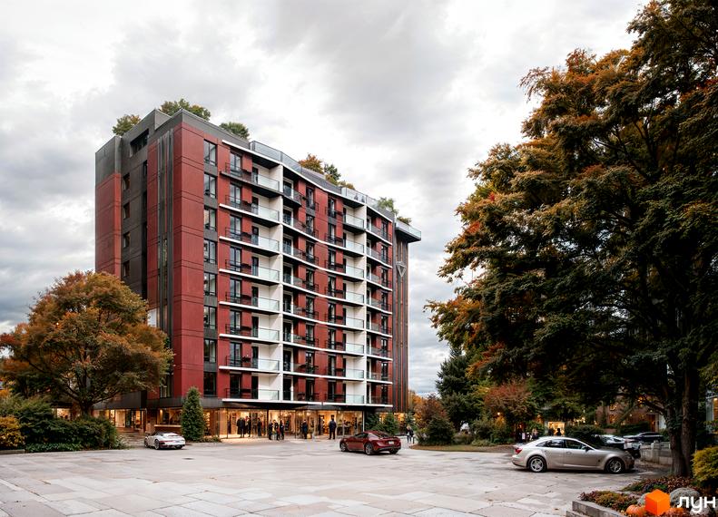 Зовнішній вигляд новобудови ЖК Рубін Апартамент з червоно-сірими фасадами та балконами. На прибудинковій території ростуть дерева та стоять автомобілі.