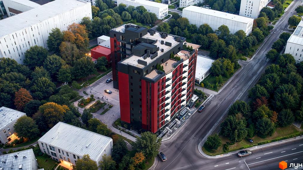 Зовнішній вигляд новобудови ЖК Рубін Апартамент з червоно-чорними фасадами та балконами. Навколо будинку розташована прибудинкова територія з деревами та дорогою.