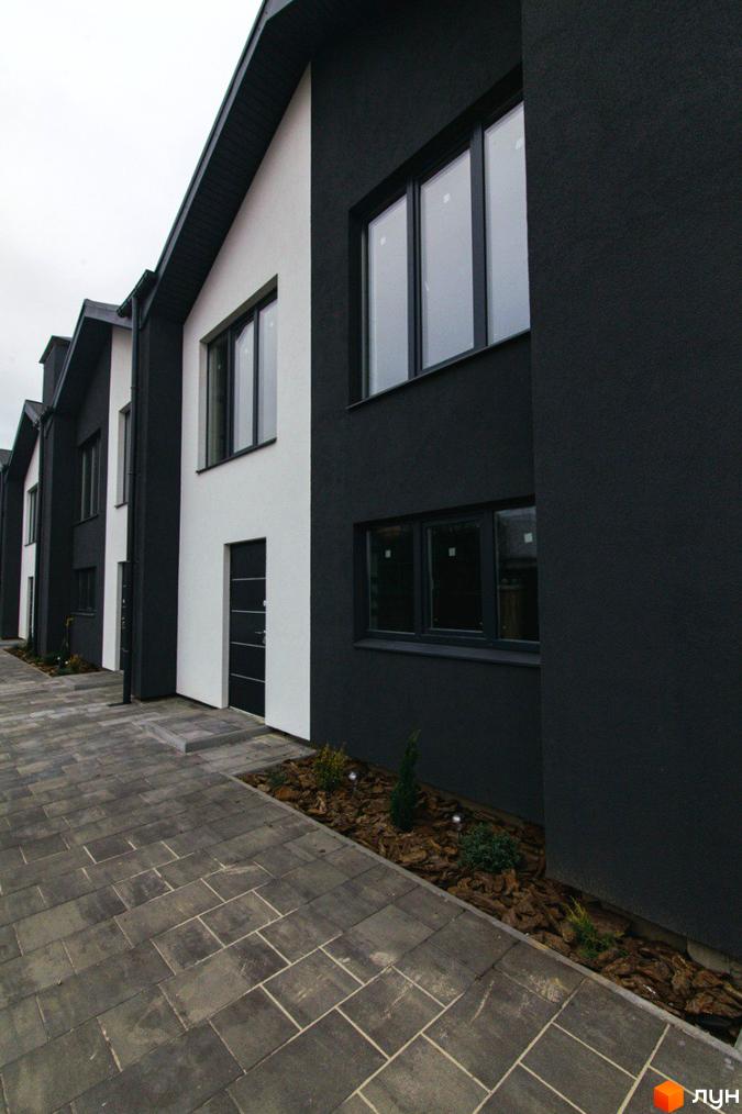 Зовнішній вигляд будинків на вулиці Шалімова, 36. Фасади чорно-білого кольору, великі вікна, тротуарна плитка та невелика зелена зона.