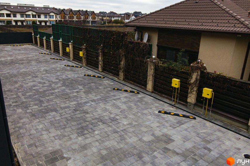 Парковка біля житлового комплексу на вулиці Шалімова, 36. Асфальтована територія з паркувальними обмежувачами та огорожею.