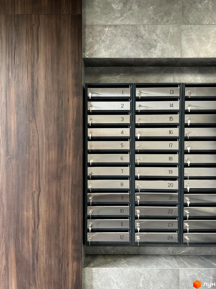 Секція з поштовими скриньками з номерами від 1 до 24 у новобудові ЖК GREENHOUSE CITY. Зовнішній вигляд фасаду з дерев'яними елементами та сірою плиткою.
