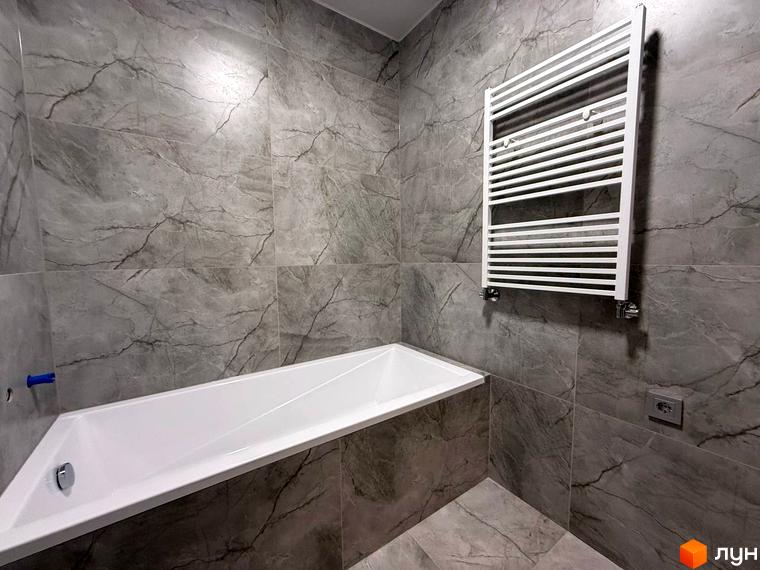 Ванна кімната в новобудові ЖК Comfort City з сірою плиткою під мармур та білою ванною.