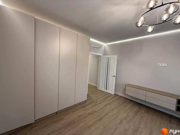Інтер'єр квартири в ЖК Comfort City з білими шафами та підсвіткою стелі. Сучасний дизайн кімнати з підлогою під дерево та телевізійною тумбою.