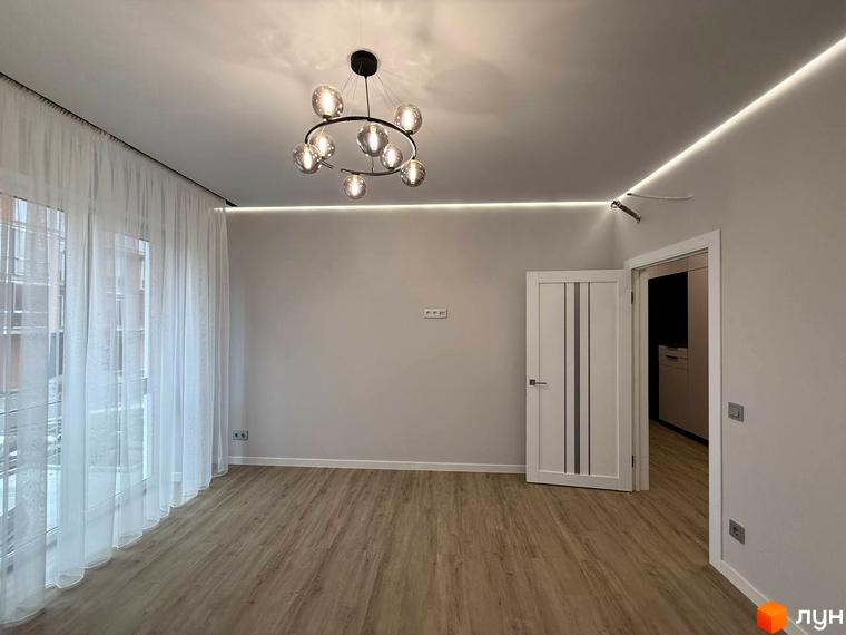 Інтер'єр квартири в ЖК Comfort City з сучасним дизайном та освітленням. Простора кімната з білими стінами, дерев'яною підлогою та великими вікнами.