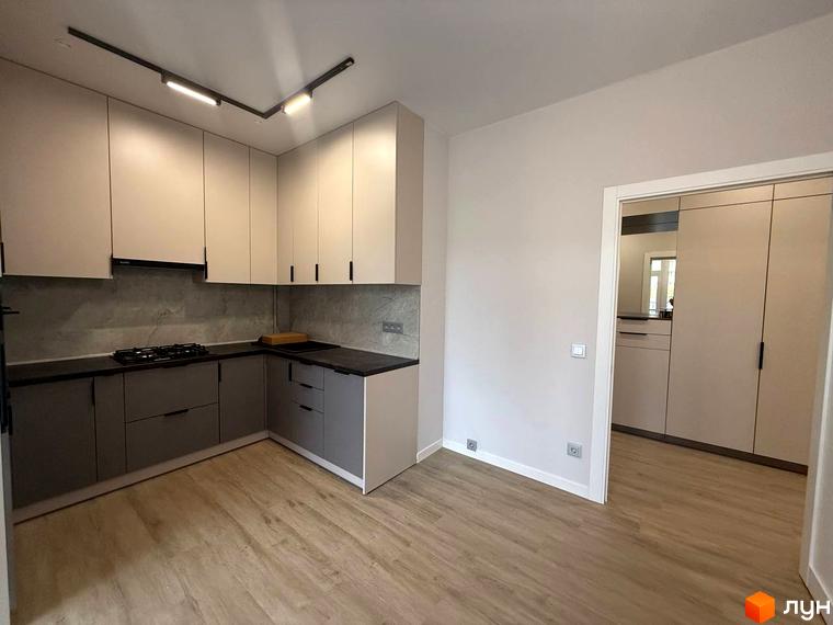Інтер'єр кухні в новобудові ЖК Comfort City з сірими та бежевими фасадами, газовою плитою та дерев'яною підлогою. Відкритий прохід до іншої кімнати з шафою.