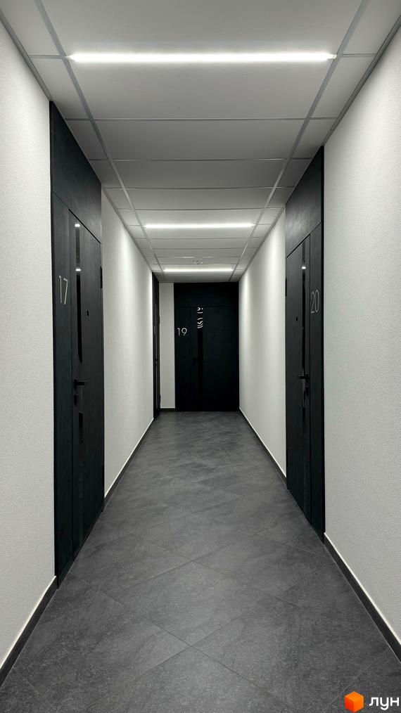 Коридор у новобудові ЖК GREENHOUSE CITY з дверима та номерами квартир. Темна підлога та білі стіни створюють мінімалістичний дизайн.