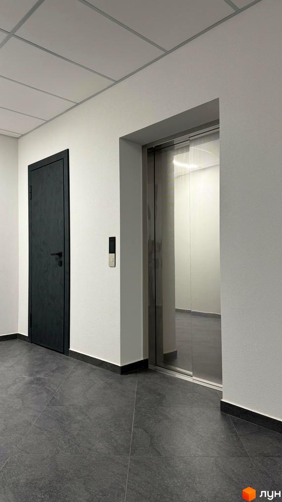 Сучасний коридор з дверима та ліфтом у житловому комплексі GREENHOUSE CITY. Сіра плитка на підлозі та білі стіни створюють мінімалістичний інтер'єр.