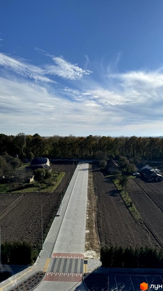 Новобудова ЖК GREENHOUSE CITY з асфальтованою дорогою та пішохідним переходом. Навколо розташовані поля та дерева.
