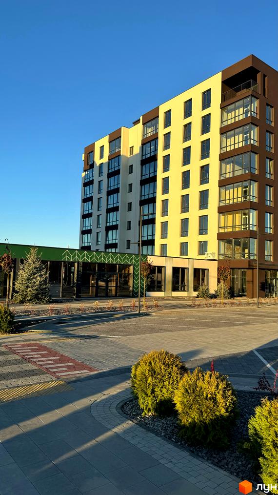 Житловий комплекс GREENHOUSE CITY з фасадом кремового та коричневого кольору, великими вікнами та зеленою зоною відпочинку. Зовнішній вигляд новобудови та прибудинкової території.