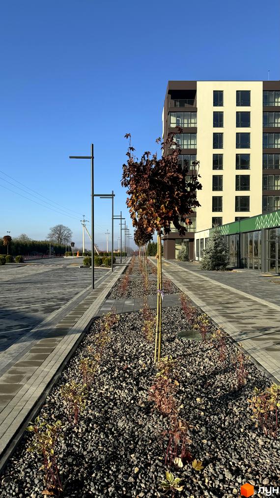 Житловий комплекс GREENHOUSE CITY з багатоповерховим будинком та доглянутою прибудинковою територією з деревами та освітленням.