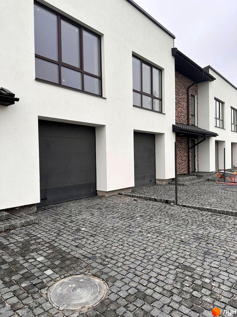 Таунхауси „Чумака“ з білими фасадами, темними вікнами та гаражними воротами. Прибудинкова територія вимощена бруківкою.