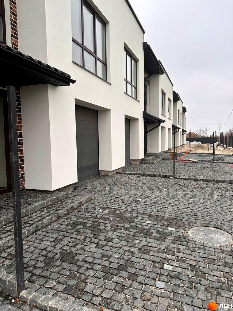 Зображення таунхаусів „Чумака“ з сірими гаражними воротами та вимощеною бруківкою прибудинковою територією.