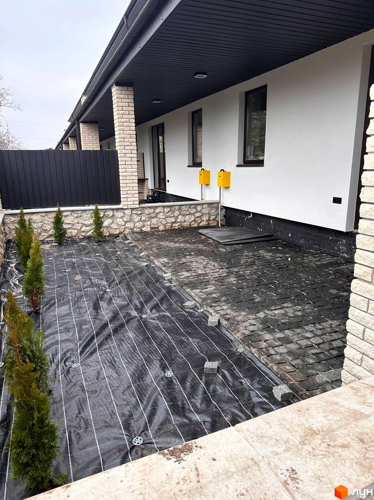 Зовнішній вигляд таунхаусу в Житловому районі „Чумака“ з прибудинковою територією, де висаджені дерева та вкладена плитка.