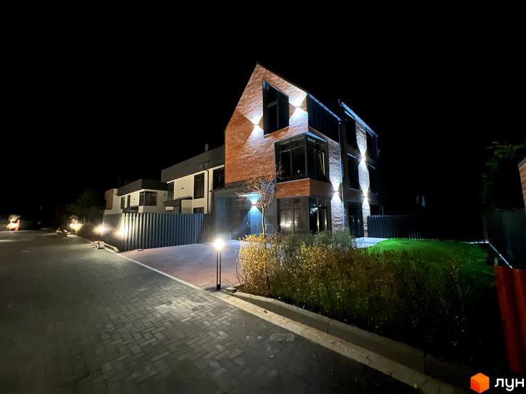 Таунхауси Lagom House у нічний час з підсвіткою фасаду та доглянутою прибудинковою територією з газоном та доріжками.