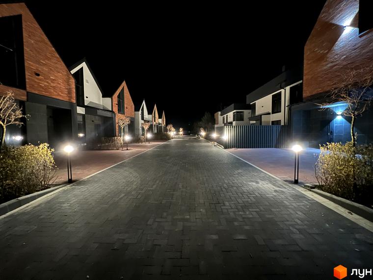 Таунхауси Lagom House з цегляним фасадом та сучасним дизайном, освітлена алея з ліхтарями та доглянутими кущами.