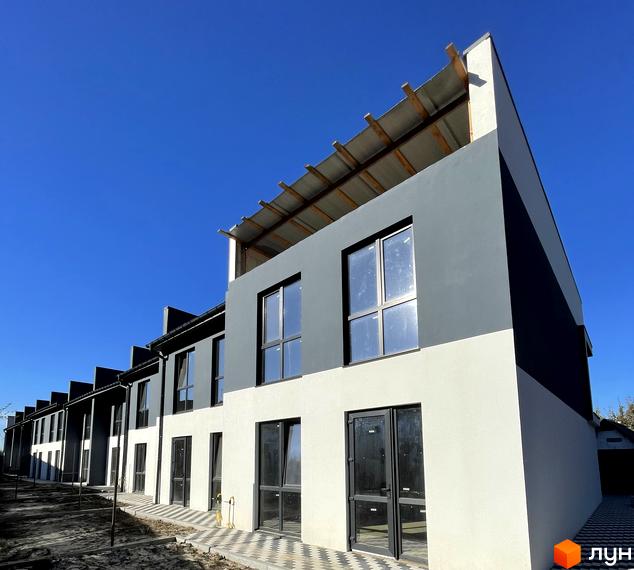 Ряд двоповерхових таунхаусів Таунхауси Belissimo з сіро-білими фасадами та великими вікнами. Перед будинками вимощена доріжка та ґрунтова ділянка.