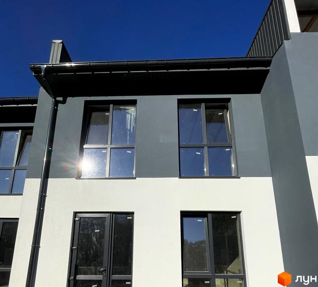 Фасад таунхаусу Belissimo з темно-сірим верхнім і світлим нижнім поверхами. На будинку встановлені вікна з темними рамами.