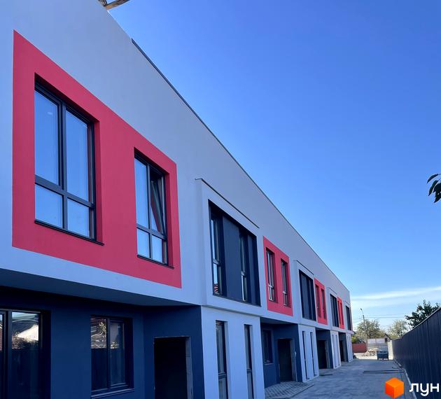 Фасад Таунхаусів Belissimo з контрастними сірими, темно-синіми та червоними блоками. Перед будинками вимощена доріжка.