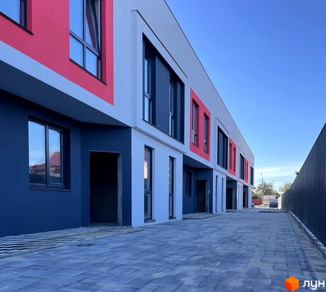 Зовнішній вигляд Таунхаусів Belissimo з фасадами білого, темно-синього та червоного кольорів. Перед будинками вимощена бруківкою територія.