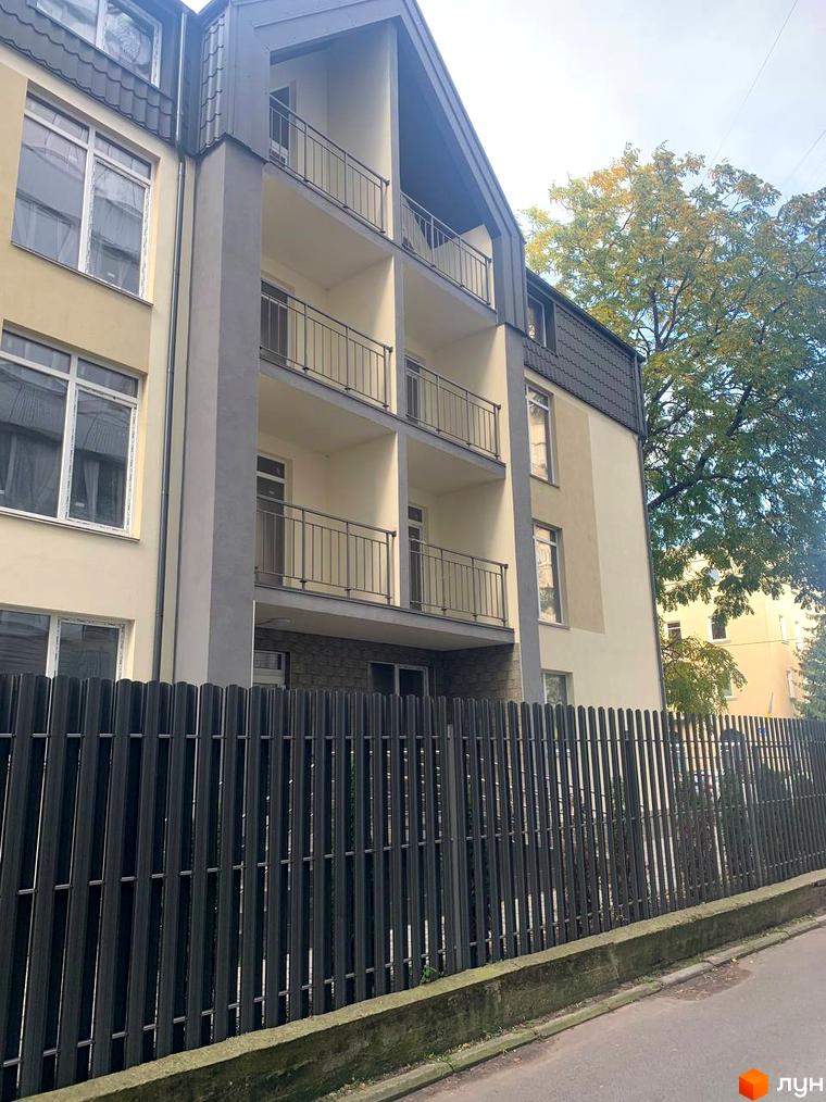 Клубний будинок „На Макіївській“ з балконами та вікнами на тлі дерева та неба. Огорожа з металевих профілів перед будинком.