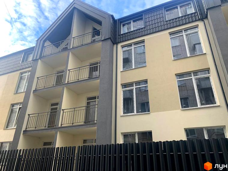 Фасад клубного будинку „На Макіївській“ з балконами та вікнами на тлі неба. Огороджена територія перед будинком.