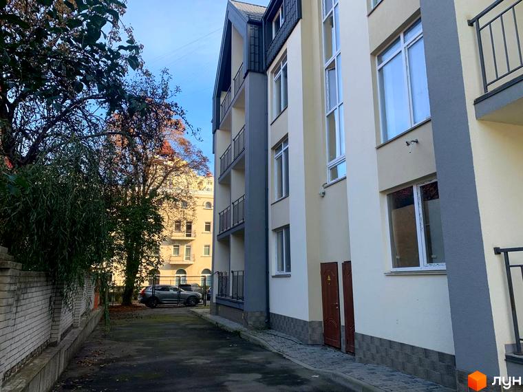 Клубний будинок „На Макіївській“ з сірими та бежевими фасадами, балконами з металевими огорожами та прибудинковою територією з деревами та автомобілем.