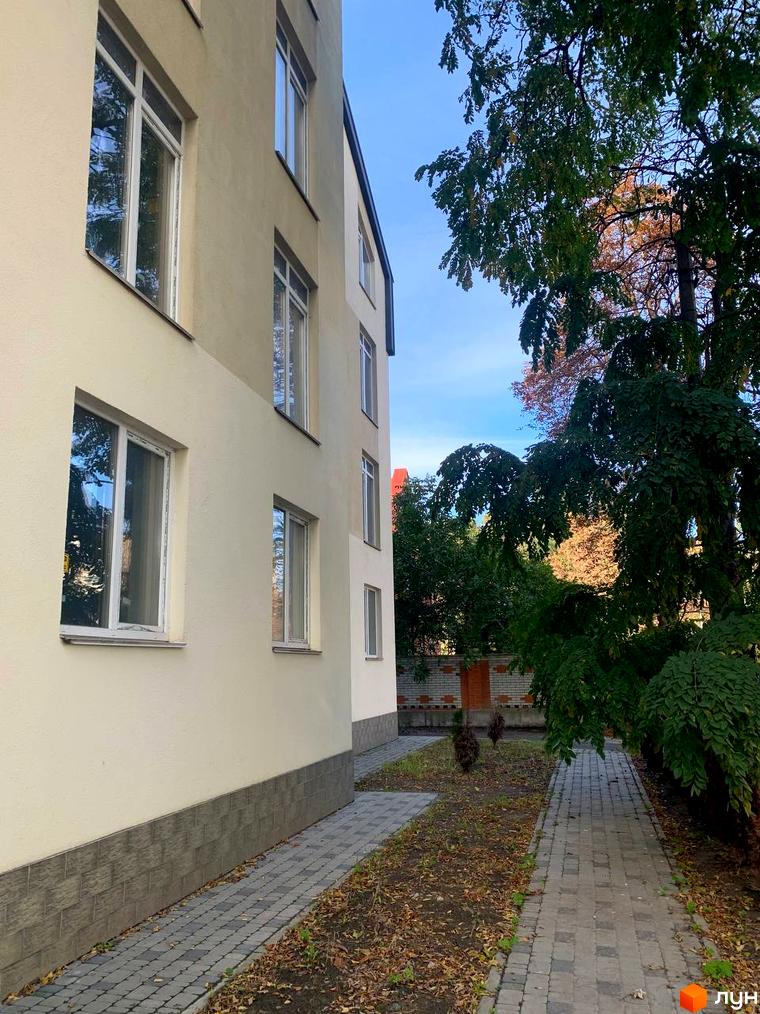 Клубний будинок „На Макіївській“ з білими вікнами та сірою плінтусною цеглою, поруч доріжка з бруківки та зелені дерева.