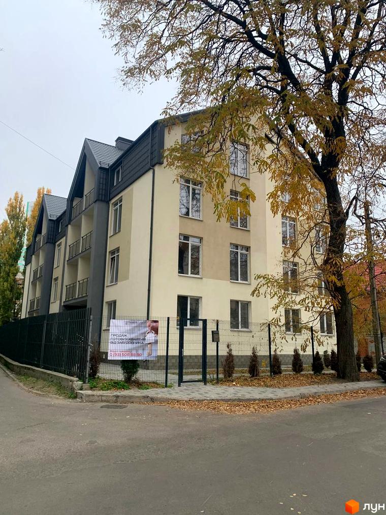 Клубний будинок „На Макіївській“ з фасадом світло-бежевого кольору та сірим дахом. Перед будинком розташована огорожа та дерева.