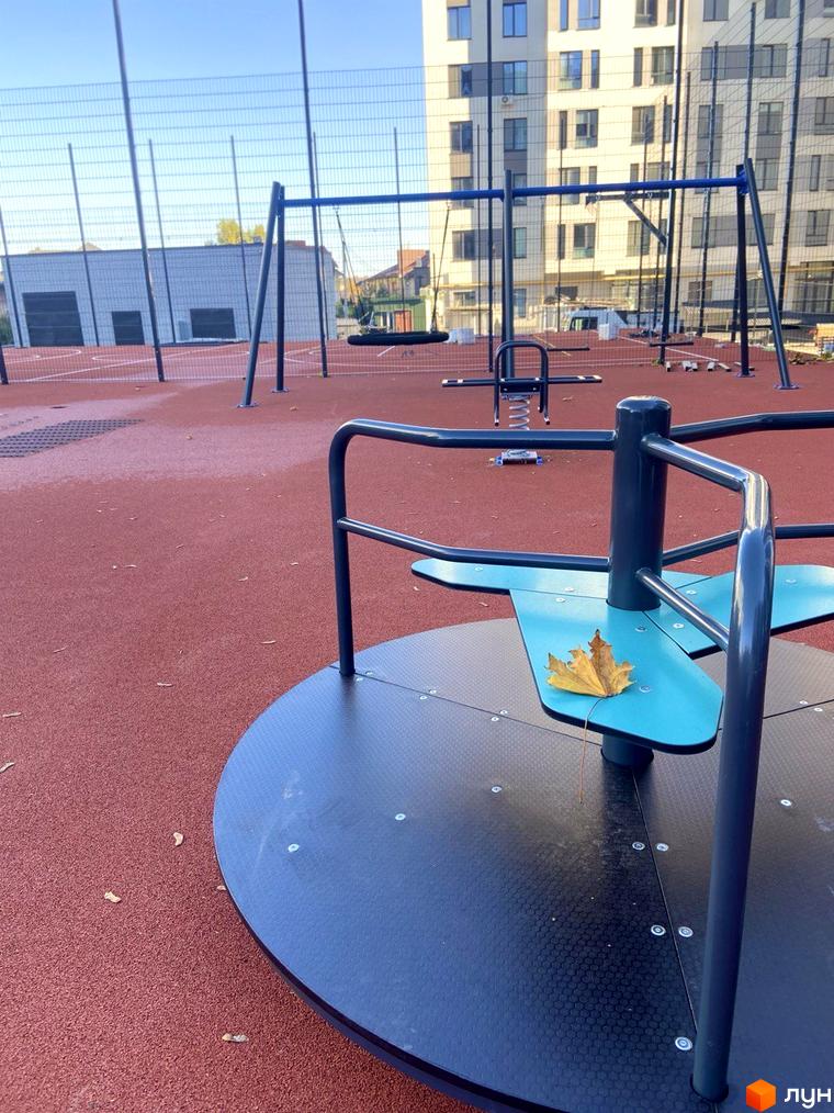 Зображення дитячого майданчика в Житловому комплексі Comfort House. На передньому плані карусель, на задньому гойдалки та будинок.