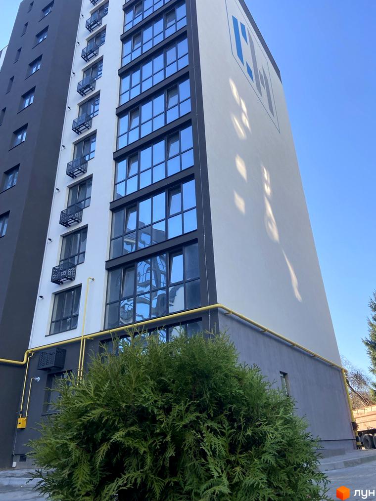 Зображення фасаду Новобудови Comfort House з великими вікнами та балконами. На передньому плані зелені насадження.