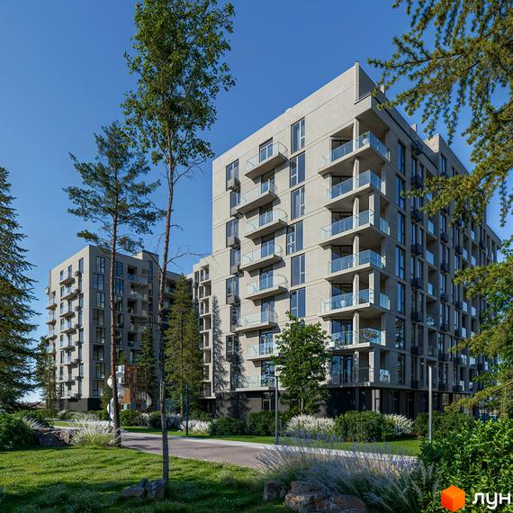 Житловий комплекс LuxAR з сірими фасадами та скляними балконами, оточений зеленню та деревами. Навколо комплексу доглянута прибудинкова територія з газонами та стежками.
