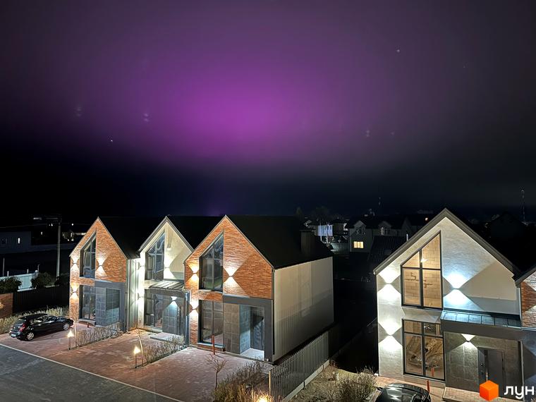 Таунхауси Lagom House з цегляним фасадом та великими вікнами, освітлені зовнішнім світлом. Прибудинкова територія з бруківкою та автомобілем.