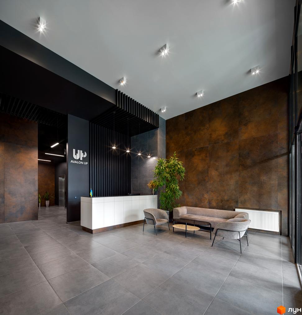 Сучасний хол житлового комплексу Avalon Up з ресепшн, зоною очікування та елегантними меблями. Оздоблення стін під метал та підлогове покриття з великої плитки створюють індустріальний стиль.