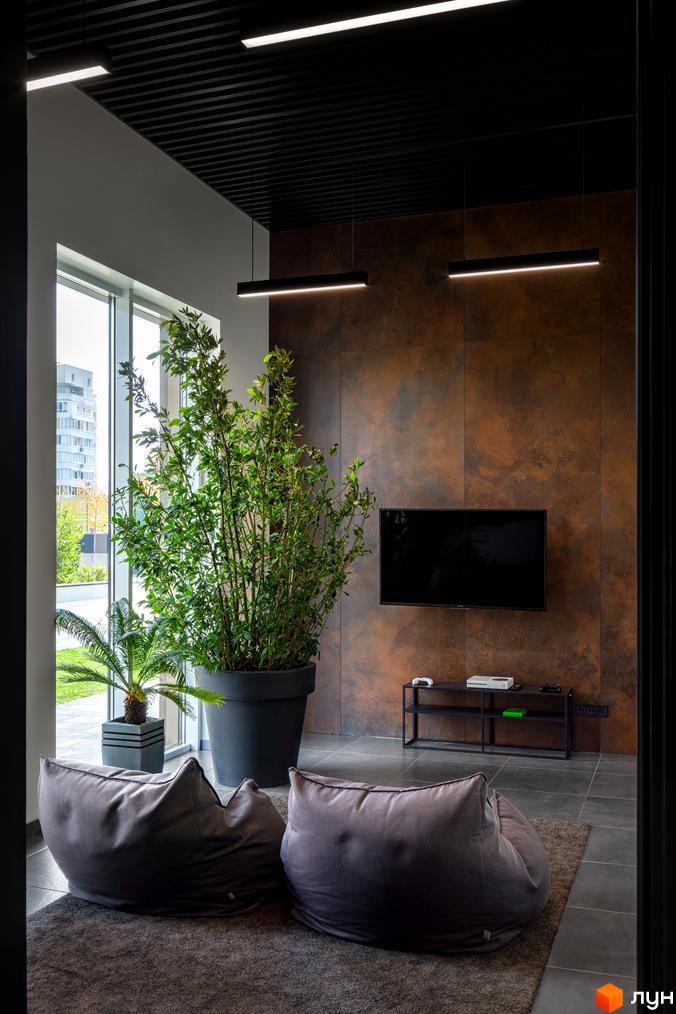 Сучасна вітальня з великим вікном, диванами-мішками та телевізором на стіні з декоративним покриттям.