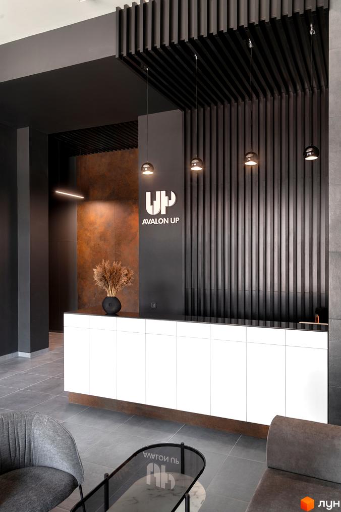 Сучасний рецепшн житлового комплексу Avalon Up з білою стійкою та декоративною стіною з вертикальних елементів. На стіні логотип Avalon Up.